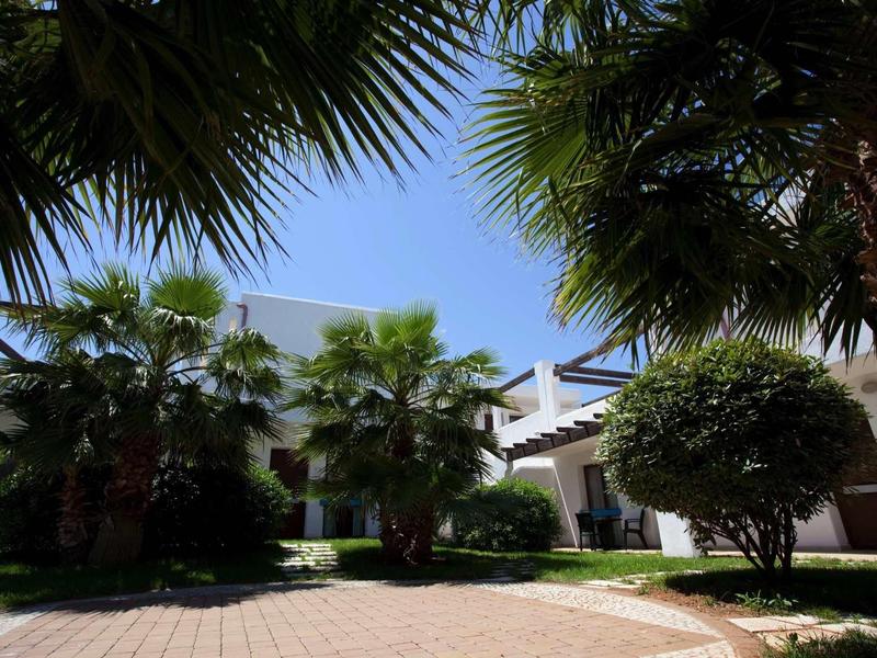 Hotel courtyard with palm trees, blue sky, and paved walkway.