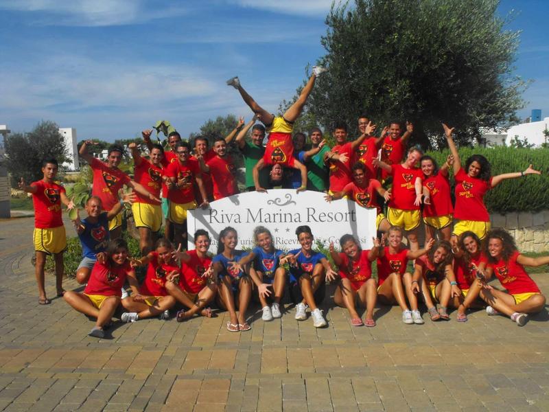 Large group of happy people in red shirts in front of resort sign outdoors.