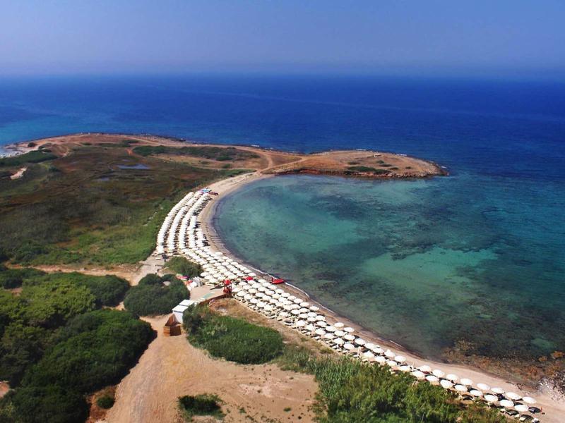 Aerial view of a coastline with a curved beach and sunbeds by the turquoise sea.
