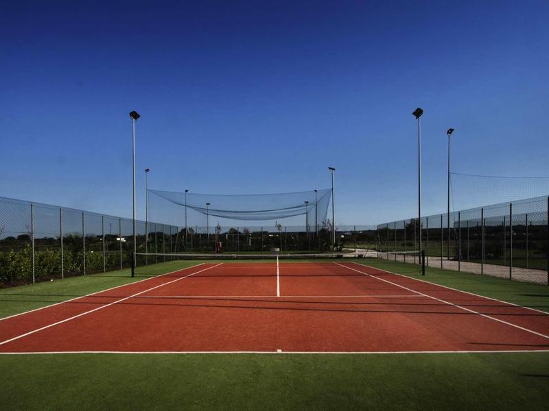 View of a red outdoor tennis court under a clear blue sky.