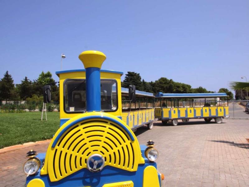 Colorful yellow-blue leisure train stands on paved path under clear sky.