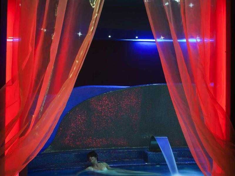 Illuminated hot tub at night with red curtains and starry light ceiling.