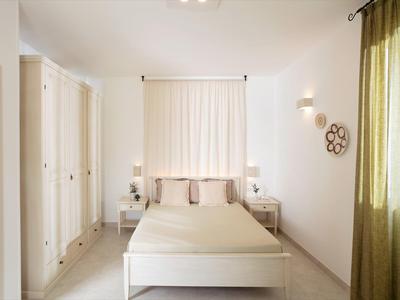 Hell eingerichtetes Schlafzimmer mit weißem Bett, Schränken und grünen Vorhängen am Fenster.