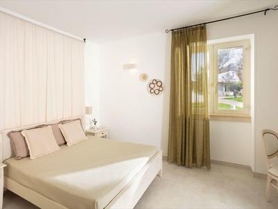 Helles Schlafzimmer mit beigem Bett, grüner transparenter Gardine und weißem Nachttisch.