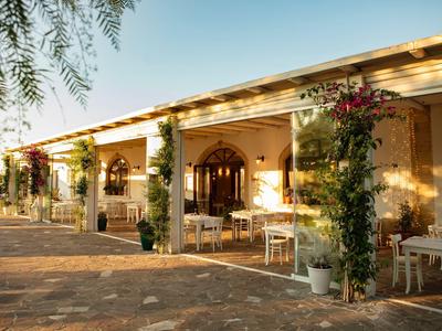 Reihenhaus mit gelber Fassade, Bögen, weißen Tischen und grünen Kletterpflanzen an Säulen.