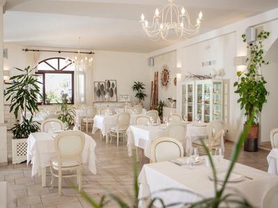 Helles, elegantes Restaurant mit weißen Tischen, Stühlen, Pflanzen und Deckenleuchter.