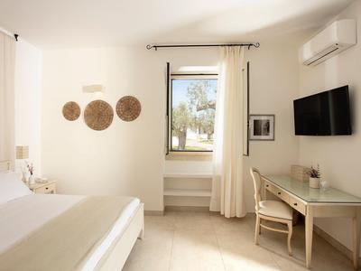 Helles Schlafzimmer mit weißer Einrichtung, Bett, Schreibtisch, Stuhl, Wanddeko und Fenster mit Vorhängen.