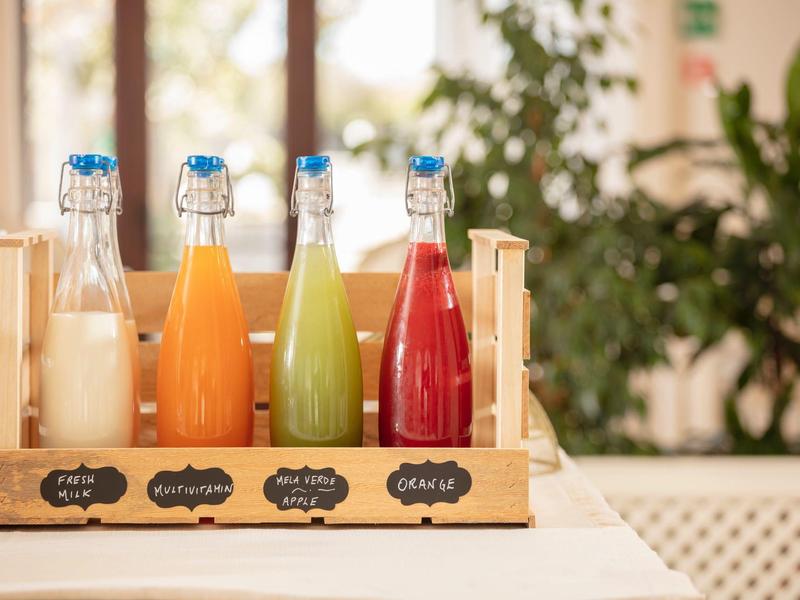 Vier Glasflaschen mit unterschiedlichen Säften stehen in einem Holzgestell auf einem hellen Tisch.