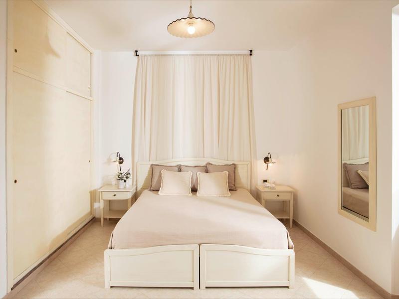 Helles Schlafzimmer mit weißem Bett, zwei Nachttischen, Vorhängen und großem Wandspiegel.