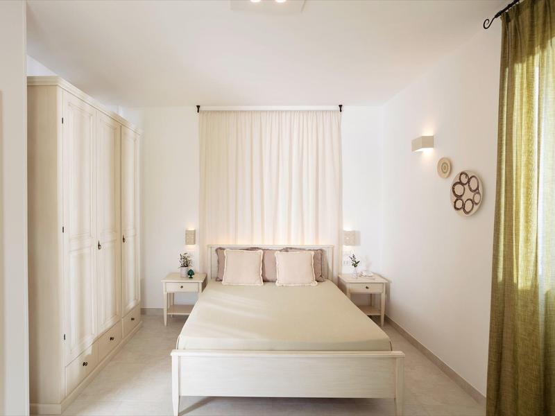 Hell eingerichtetes Schlafzimmer mit weißem Bett, Schränken und grünen Vorhängen am Fenster.