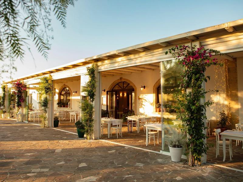 Reihenhaus mit gelber Fassade, Bögen, weißen Tischen und grünen Kletterpflanzen an Säulen.