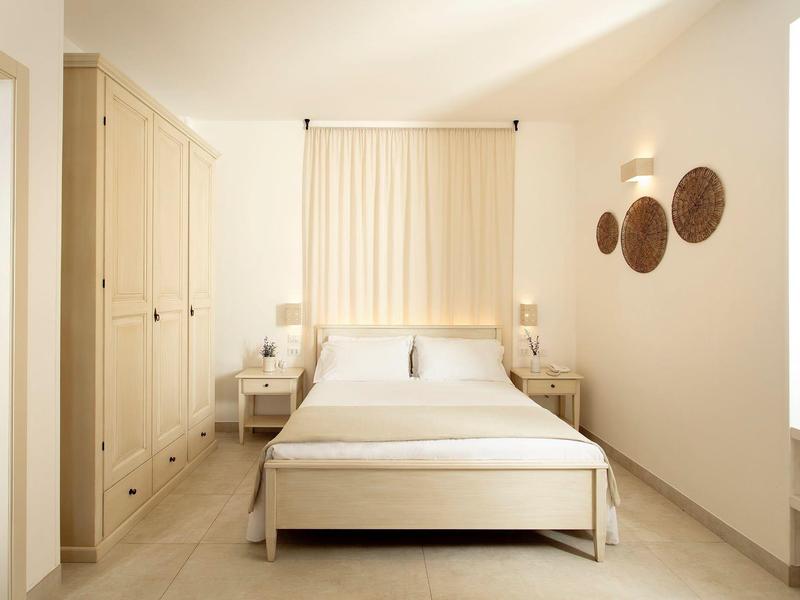 Helles Schlafzimmer mit weißem Bett, Vorhängen, Nachttischen und Wanddekoration aus Holz.