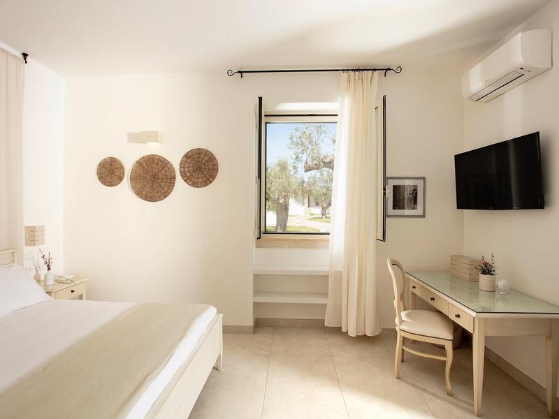 Helles Schlafzimmer mit weißer Einrichtung, Bett, Schreibtisch, Stuhl, Wanddeko und Fenster mit Vorhängen.