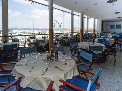 Hell eingerichteter Speisesaal mit blauen Stühlen und Blick auf den Hafen durch große Fenster.