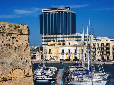 Moderne Glasfassade neben alten Gebäuden und Yachthafen unter blauem Himmel.