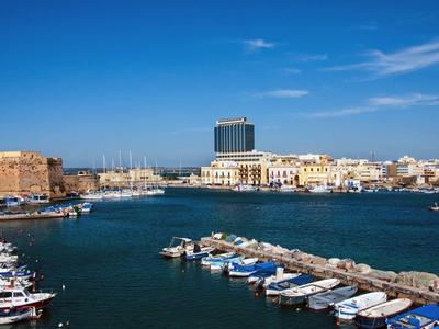 Blick auf einen Hafen mit Booten und einem modernen Hotel am Ufer unter blauem Himmel.