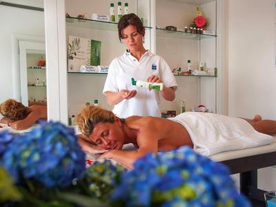 Frau entspannt auf Massagetisch, Therapeutin bereitet Behandlung in hellem Raum vor.