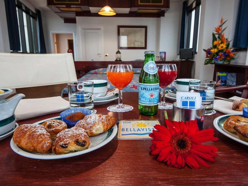 Tisch mit Frühstück, Croissants, Wasser, Getränken, Blumen und hellem Esszimmer im Hintergrund.