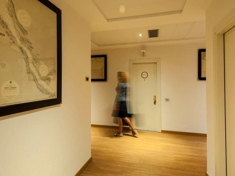 Flur mit hellen Wänden, Holzboden, mehreren Türen und einem unscharfen Mann in Bewegung.