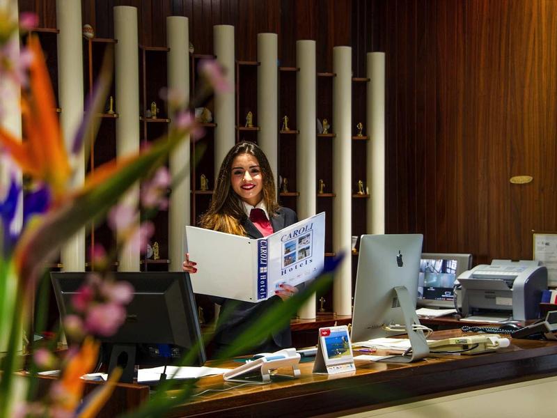 Eine Frau steht hinter einem Empfangstresen in einem modern eingerichteten Büro mit Holzvertäfelung.