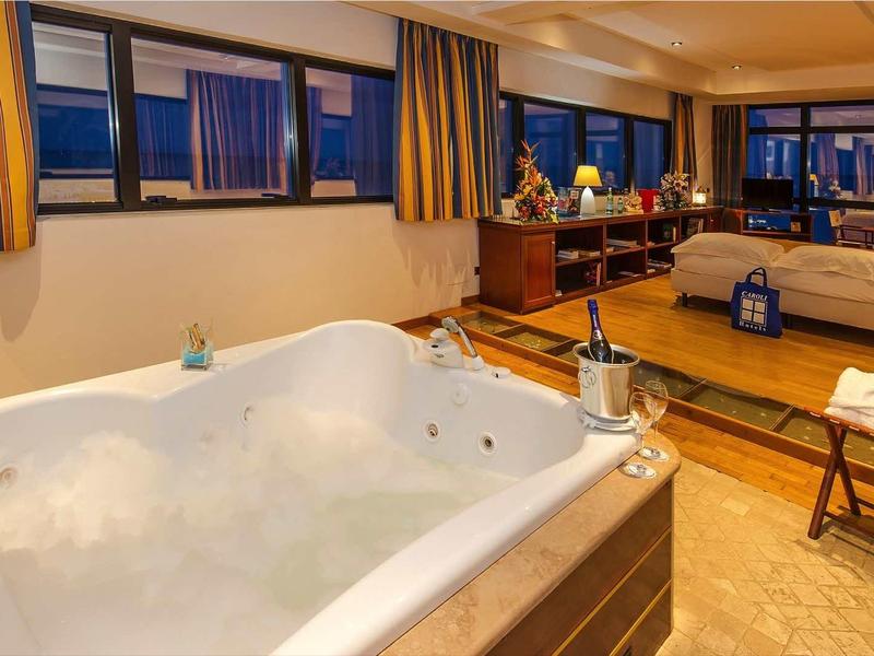 Luxuriöses Hotelzimmer mit großem Whirlpool, Doppelbett, Holzboden und dunklen Vorhängen.