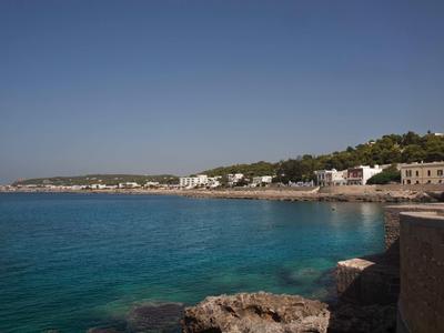 Klares blaues Meer, felsige Küste und Häuser am Hang unter klarem Himmel an einer Bucht.