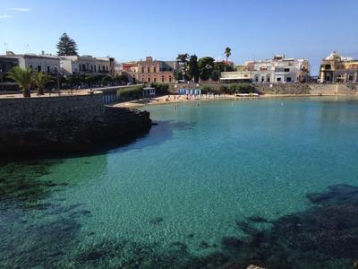 Klares türkisfarbenes Wasser in einer Bucht vor einer kleinen Stadt mit weißen Gebäuden und blauem Himmel.