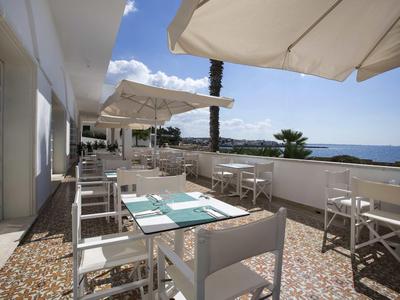 Terrasse mit weißen Tischen und Stühlen, Sonnenschirmen, Meerblick und blauem Himmel.