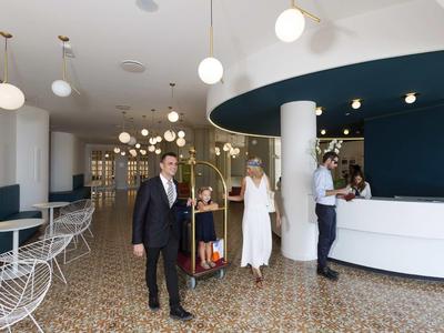 Modernes Hotel-Lobby mit weißem Empfangstresen, runden Lampen und mehreren Gästen in eleganter Kleidung.