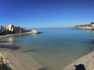 Kleiner ruhiger Meeresarm mit Sandstrand, bebauten Uferpromenaden und klarem blauem Himmel.