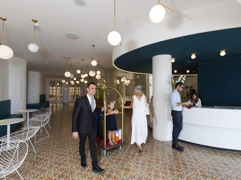 Modernes Hotel-Lobby mit weißem Empfangstresen, runden Lampen und mehreren Gästen in eleganter Kleidung.