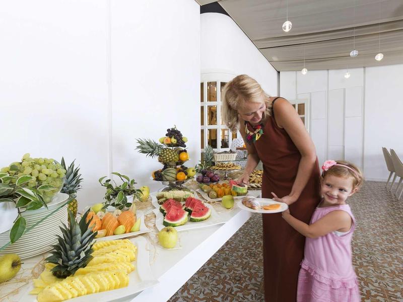 Frau und Mädchen nehmen Obststücke von Buffet mit farbenfrohen Früchten auf weißem Tisch.