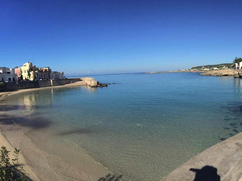 Kleiner ruhiger Meeresarm mit Sandstrand, bebauten Uferpromenaden und klarem blauem Himmel.