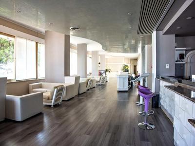 Heller, moderner Raum mit weißen Sesseln, Holzboden und Bar mit lila Hockern.