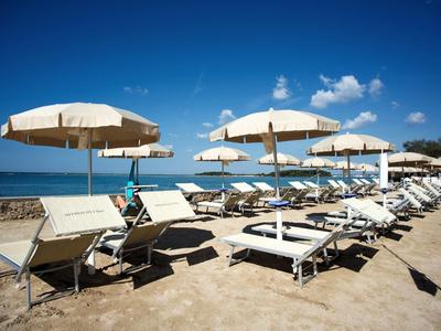 Strand mit weißen Sonnenschirmen und Liegestühlen, blauer Himmel und ruhiges Meer im Hintergrund.