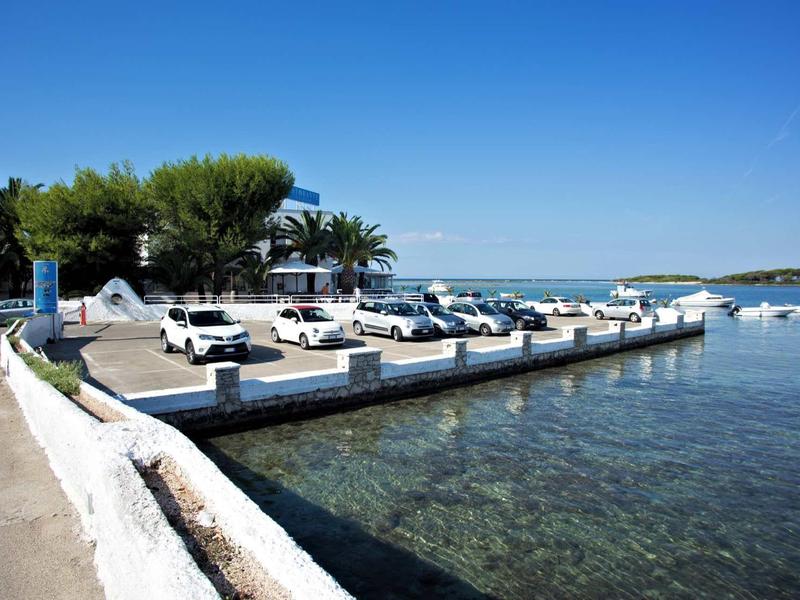 Kleiner Hafen mit weißen Booten, klaren Gewässern und blauem Himmel, umgeben von Bäumen.