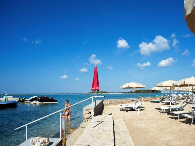 Strand mit Boot, Sonnenschirmen, Liegestühlen und blauem Himmel mit Wolken am Meer.