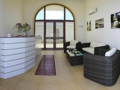 Heller Wartebereich mit runder Theke, schwarzen Korbmöbeln und großem Bogenfenster.