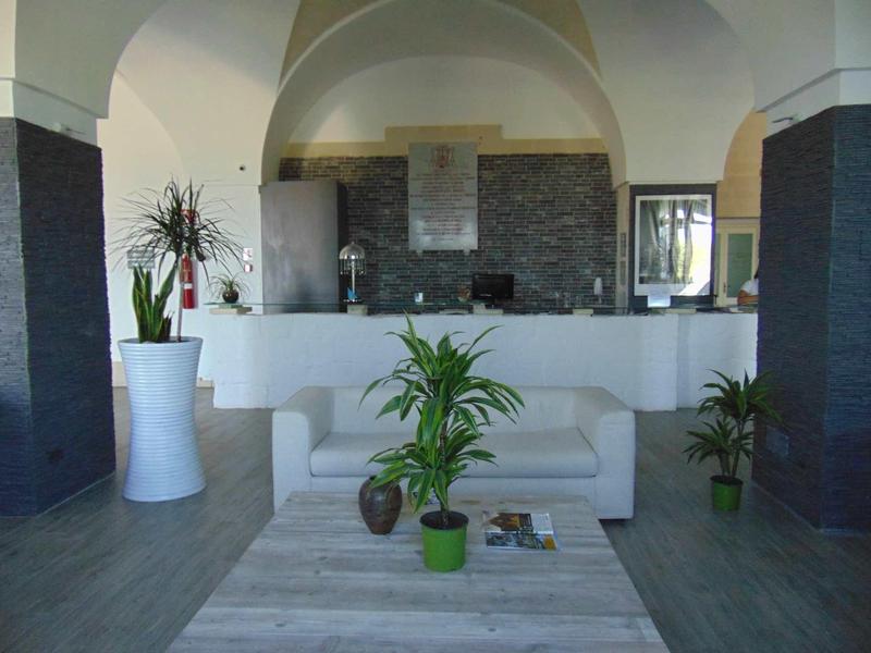 Simple hotel lounge with white sofa, plants, and modern stone counter backdrop.