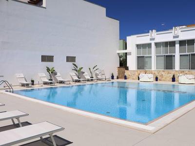 Moderner Außenpoolbereich mit Liegestühlen und weißen Wänden bei klarem Himmel.