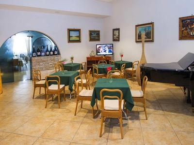 Großer Raum mit Tischen, Stühlen, grünem Stoff, Klavier und Wandbildern, heller Bodenfliese.