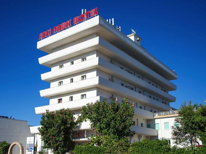 Mehrstöckiges weißes Hotelgebäude mit roten Buchstaben auf dem Dach, umgeben von Bäumen.