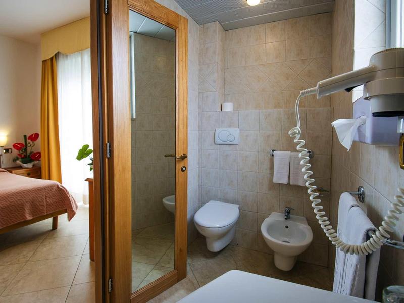 Kleines Badezimmer mit Toilette, Bidet, Haartrockner und Blick ins Schlafzimmer mit orangefarbenem Bett.