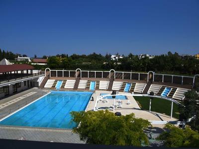 Außen-Schwimmbad mit blauer Wasserfläche, Liegestühlen und grünem Rasen unter klarem blauem Himmel.