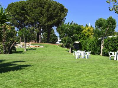 Jardín verde con sillas y mesas bajo árboles en un día soleado