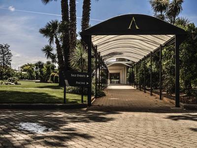 Pasillo cubierto con bancos que atraviesa un jardín con palmeras y otras plantas.
