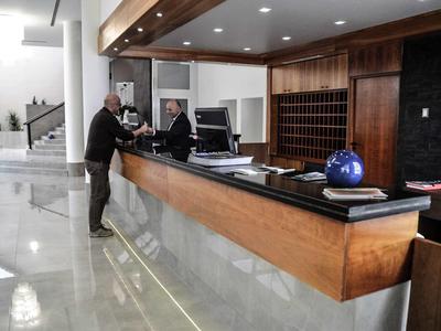 Moderne Hotellobby mit Holztheke, zwei Männern beim Gespräch und heller Marmorfußboden.