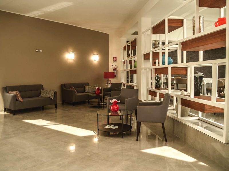 Hell beleuchteter Raum mit grauen Sesseln, Regalen und modernem Bodenbelag aus Steinfliesen.