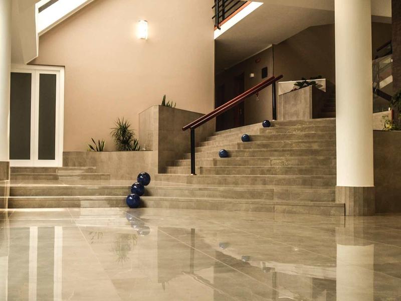 Moderner Raum mit hellen Marmorstufen, Glasfenstern, Pflanzen und reflektierendem Boden.