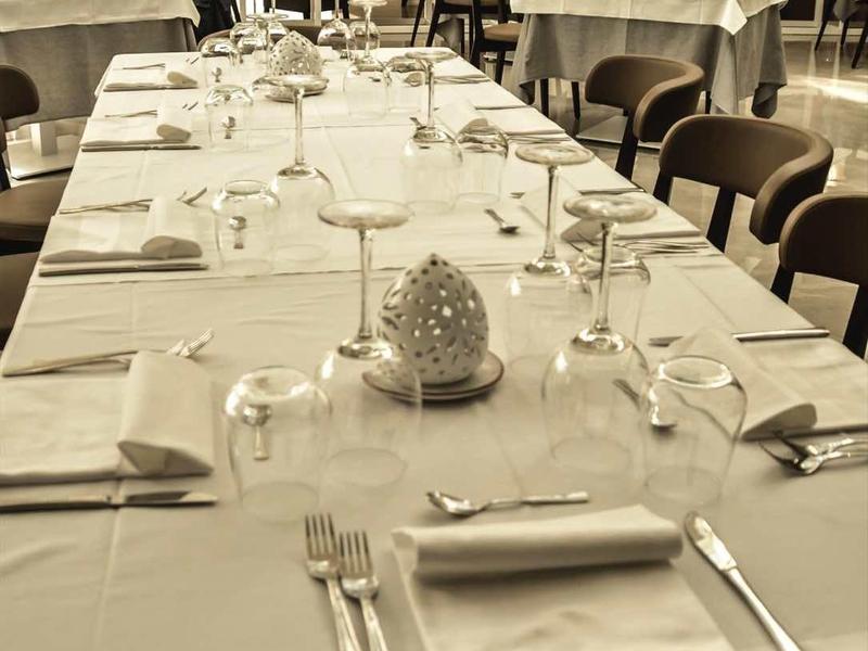 Ein festlich gedeckter langer Tisch mit weißen Tüchern, Gläsern und Besteck in einem Restaurant.